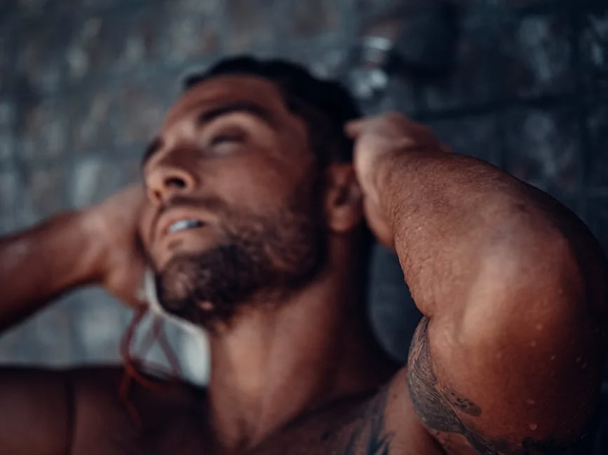 Close-up of a muscular, tattooed man enjoying a refreshing shower.